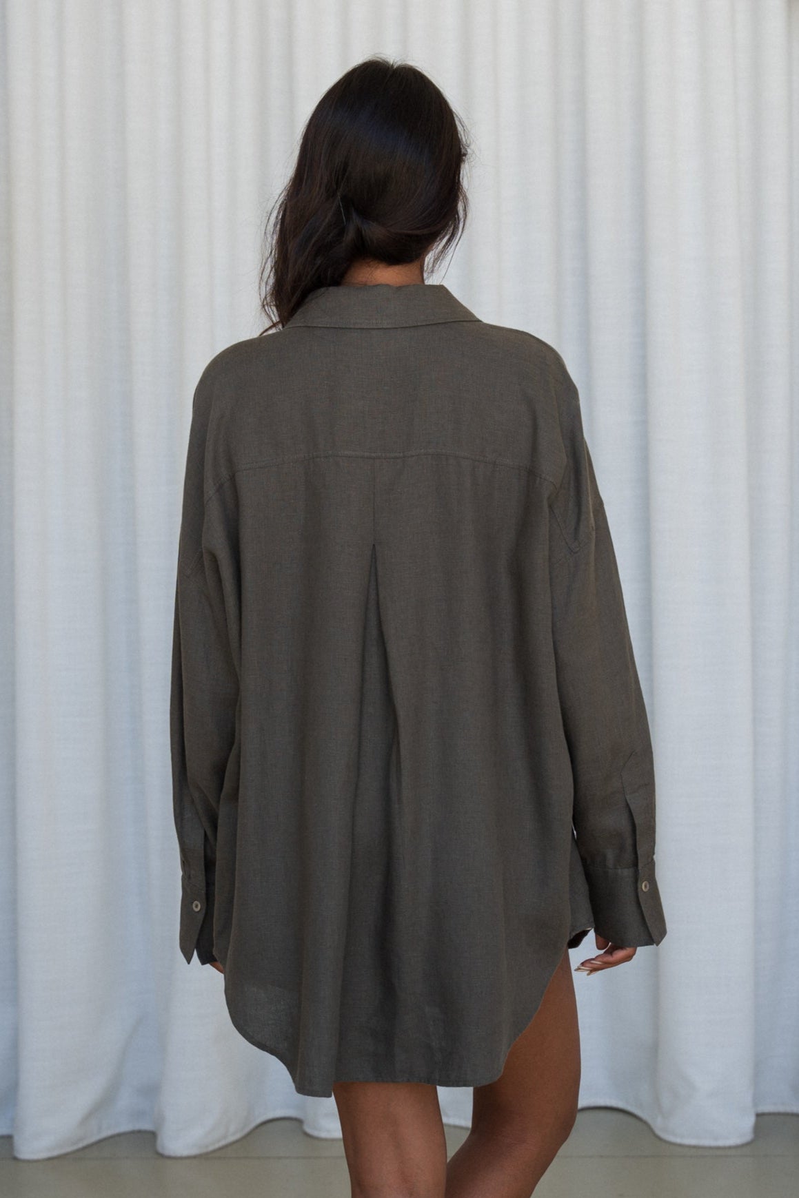 LILY PILLY woman wearing a khaki Kirra linen shirt back view against a white curtain background