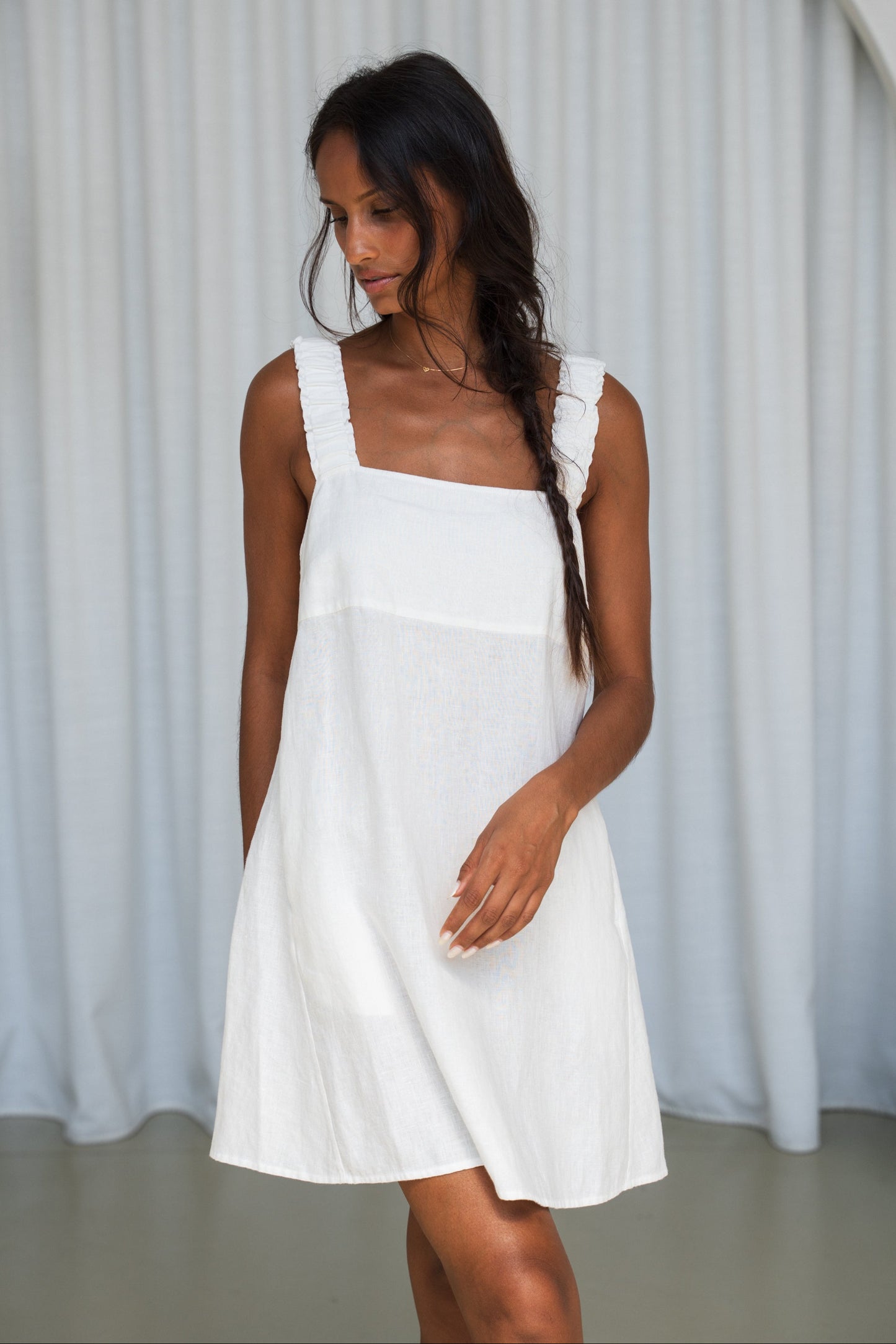 LILLY PILLY woman in an ivory Zahra linen dress showing front view while standing in front of a white curtain background