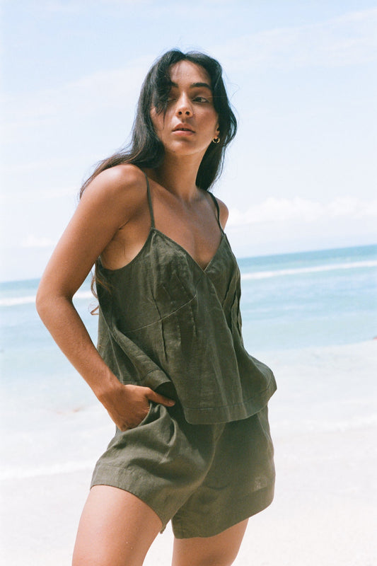 LILLY PILLY woman wearing a khaki Bea linen cami top and Gaia shorts outfit on a beach with clear blue sky.