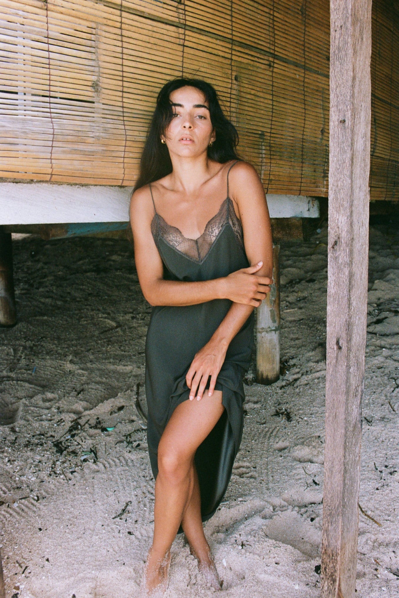 Woman wearing a khaki Freya silk slip dress with lace details against a rustic background
