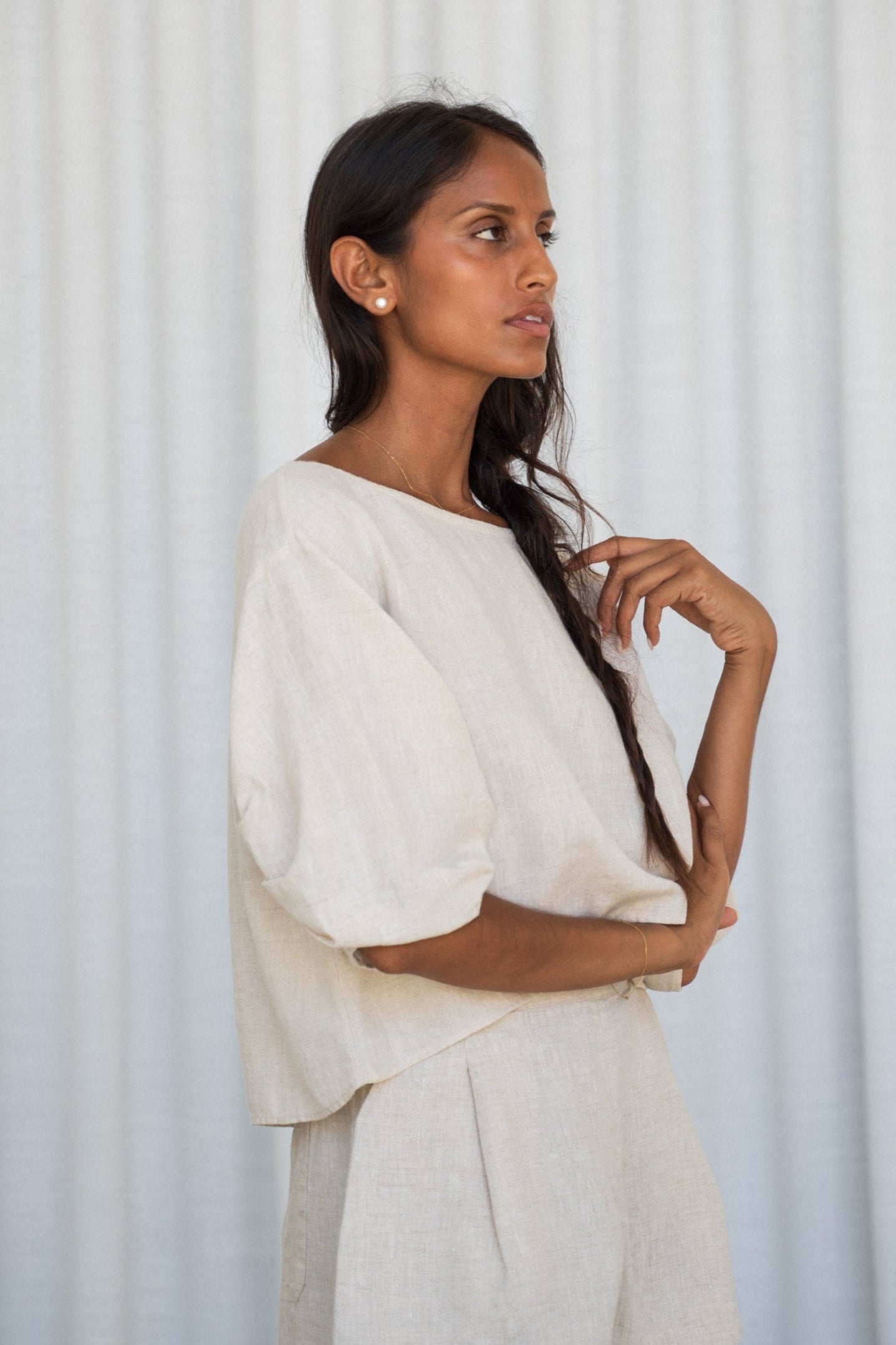 Woman wearing a oatmeal Leia linen top showing side view against a light gray background
