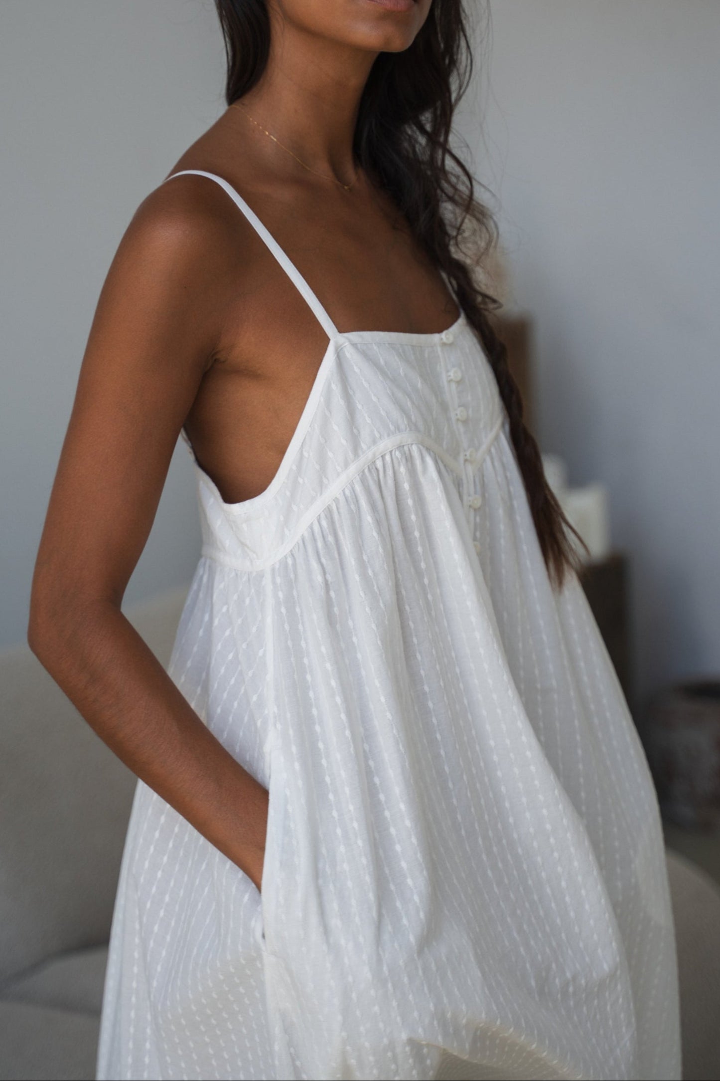 Woman wearing a white dress with thin straps against a neutral background
