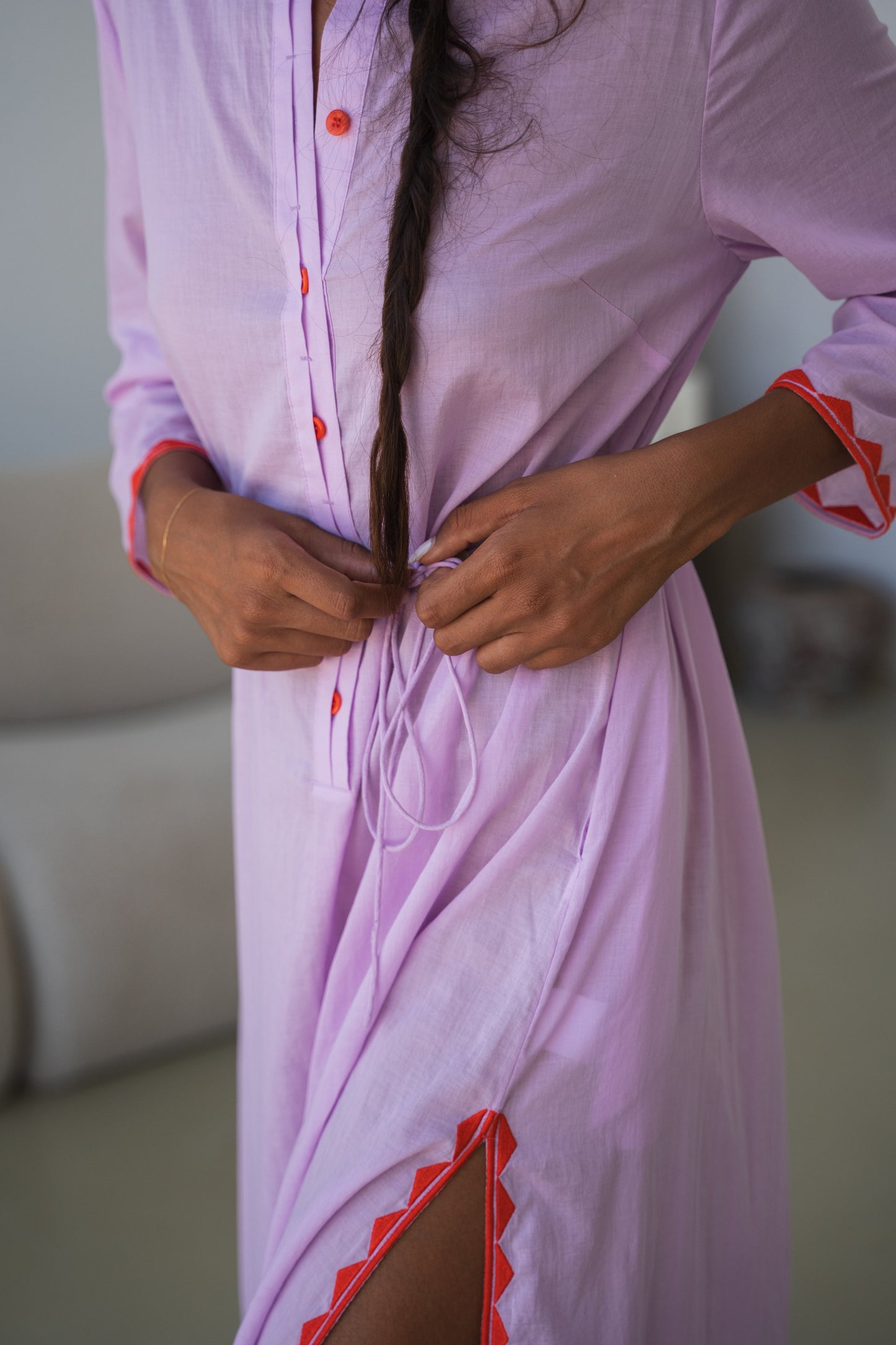 LILLY PILLY woman in a orchid Callie cotton dress standing side view showing waist tie details in a minimalistic room.