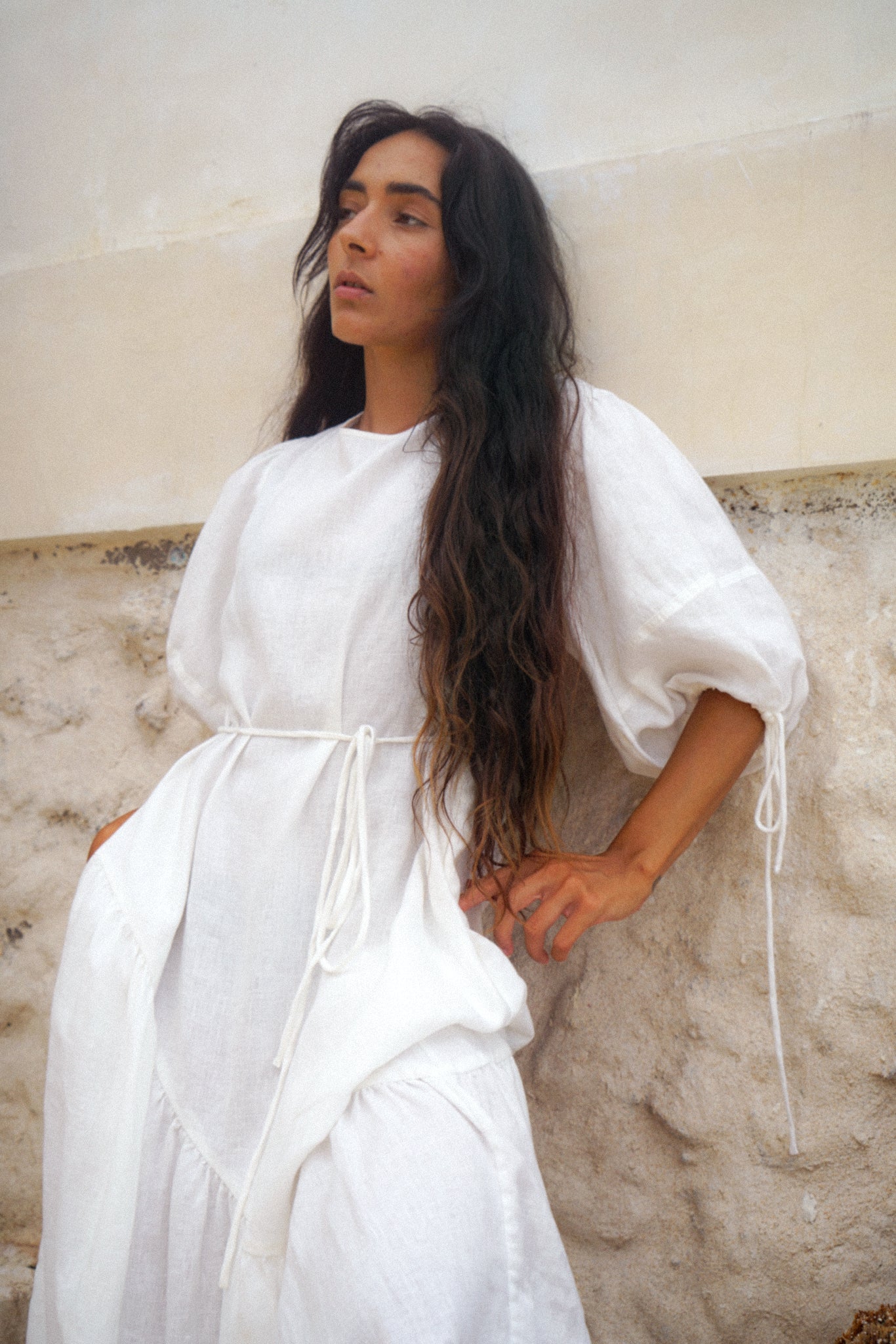 LILLY PILLY woman wearing Charlotte linen dress in Ivory standing by a white textured wall