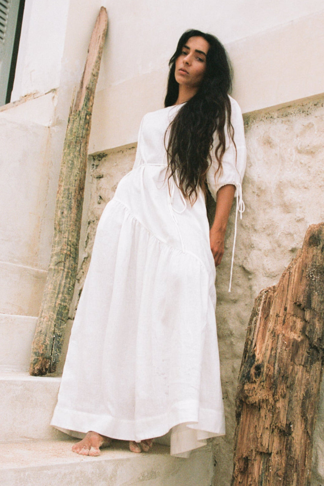 LILLY PILLY woman wearing Charlotte linen dress in Ivory standing by a white textured wall