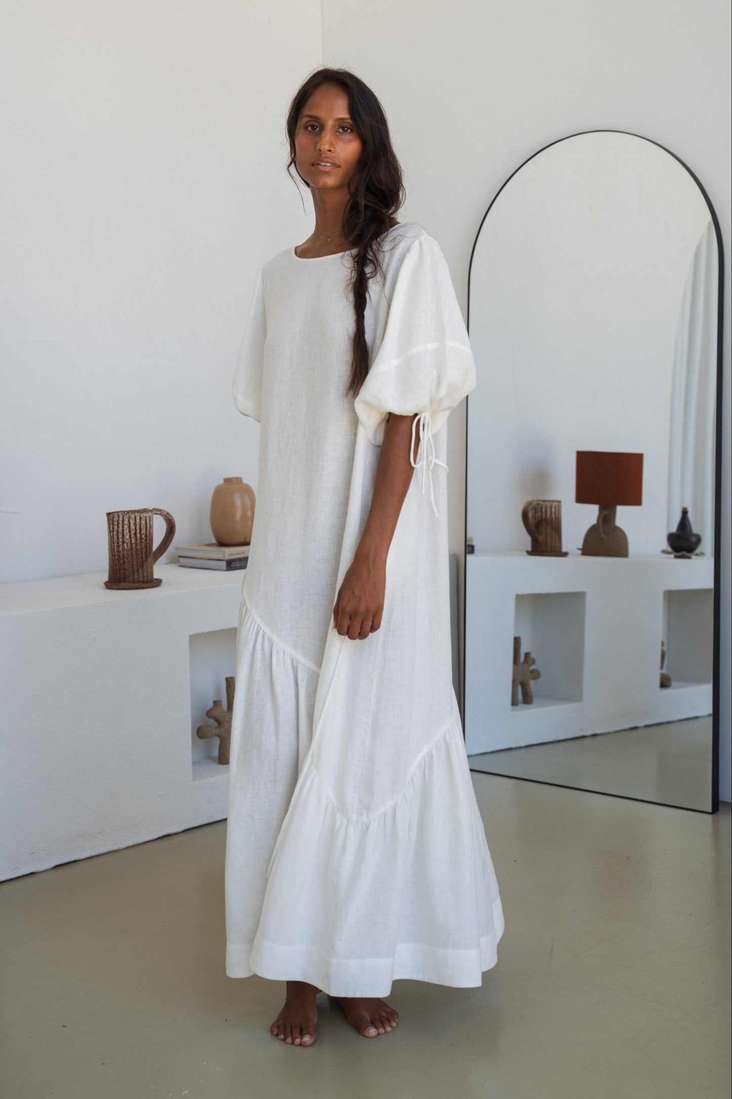 LILLY PILLY woman wearing Charlotte linen dress in Ivory standing by a mirror