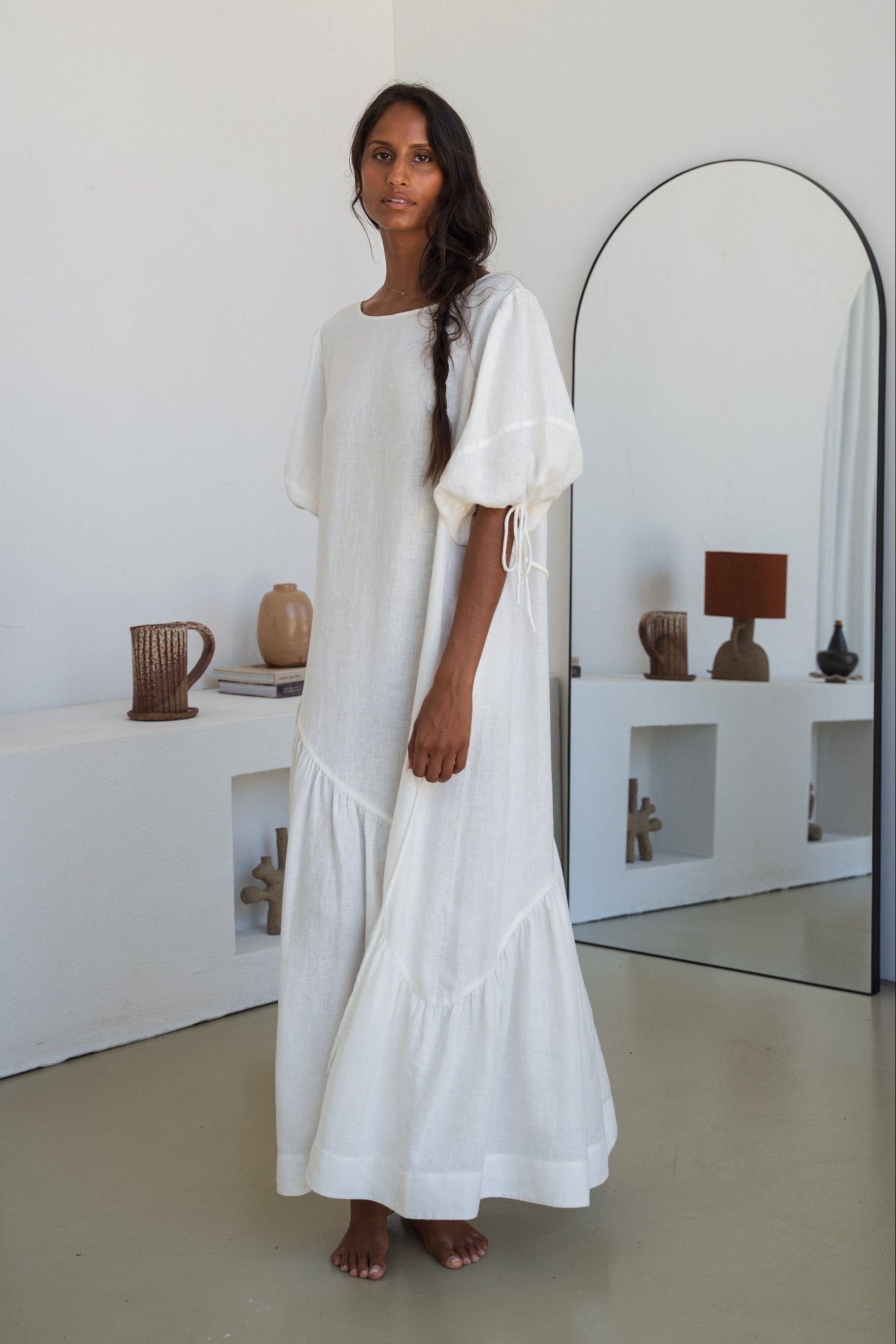 LILLY PILLY woman wearing Charlotte linen dress in Ivory standing by a mirror