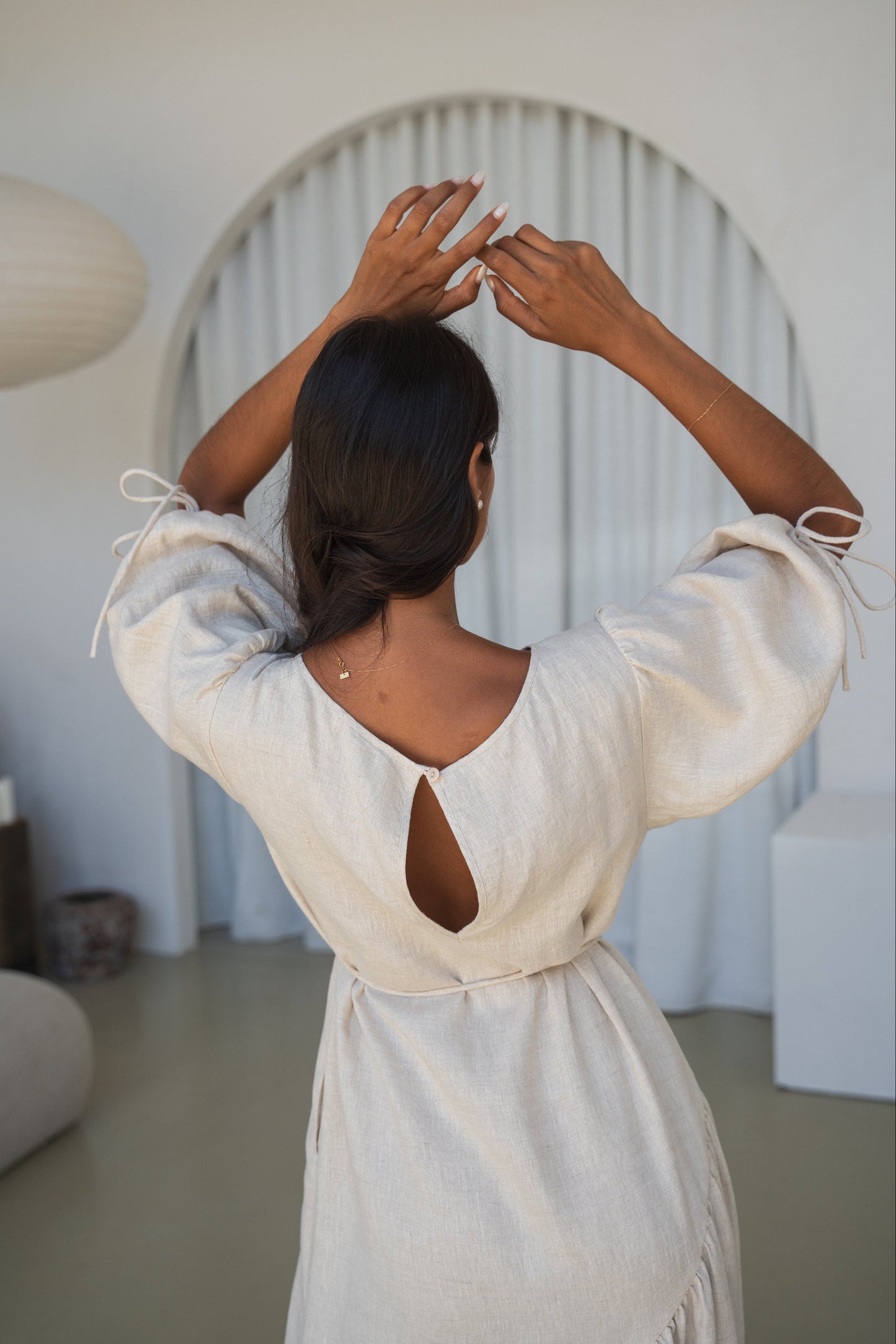 LILLY PILLY woman in an oatmeal Charlotte linen dress back view close up while standing in a minimalistic room