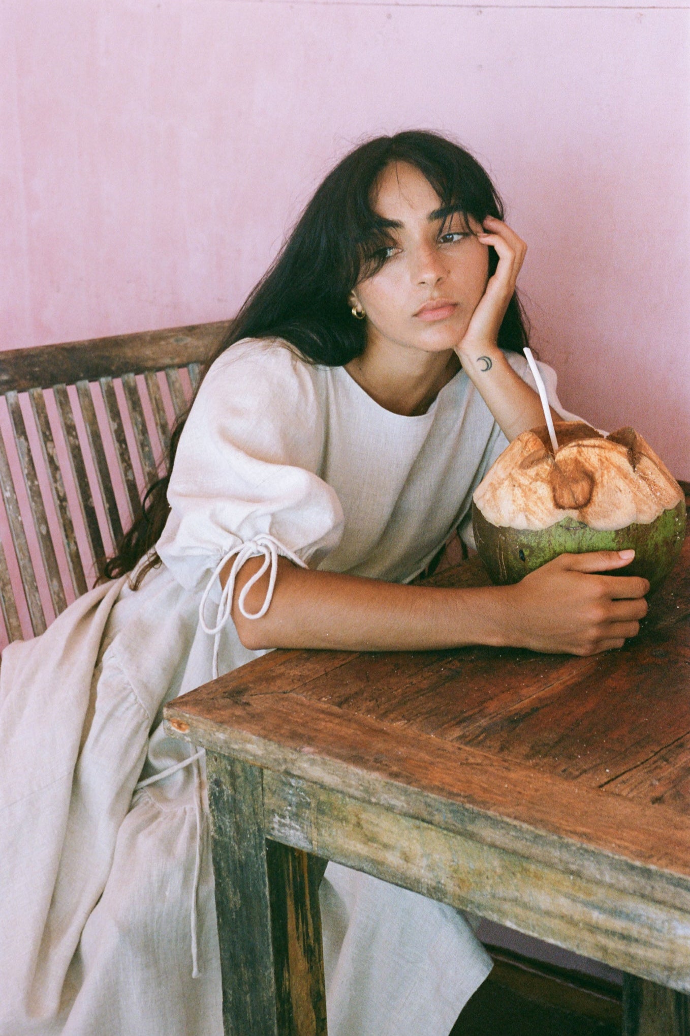 LILLY PILLY woman in an oatmeal Charlotte dress sitting on a chair at a wooden table.