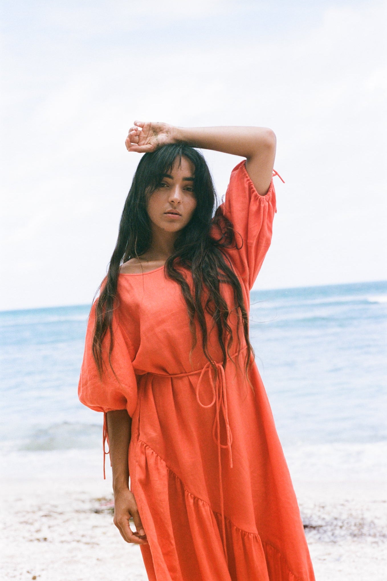 LILLY PILLY woman wearing a spritz coloured Charlotte linen dress on the sand by the water