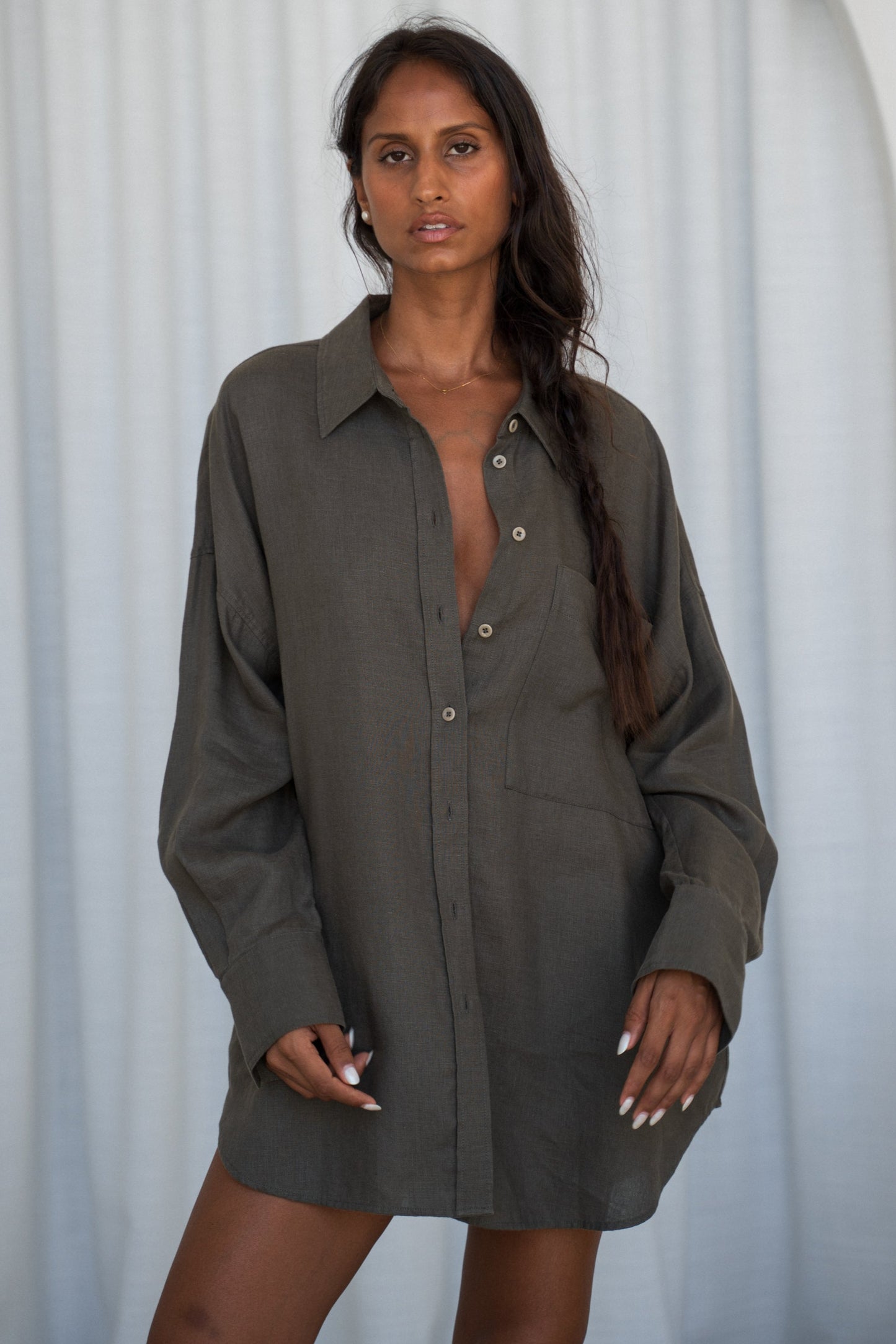 LILY PILLY woman wearing a khaki Kirra linen shirt against a white curtain background