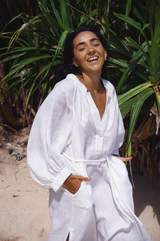 Woman in an ivory Mae linen dress standing in front of green plants