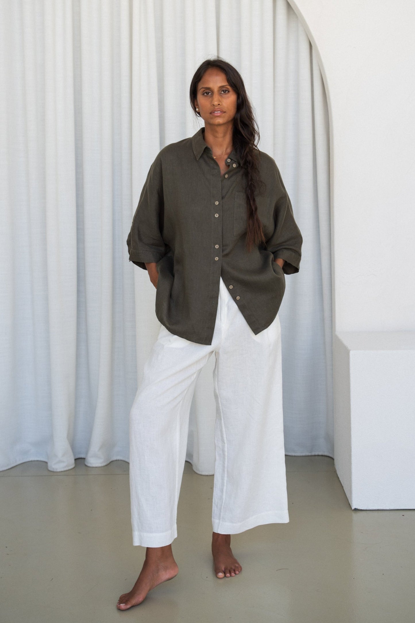 LILLY PILLY woman wearing a khaki Pixie linen shirt and white linen pants outfit by an archway