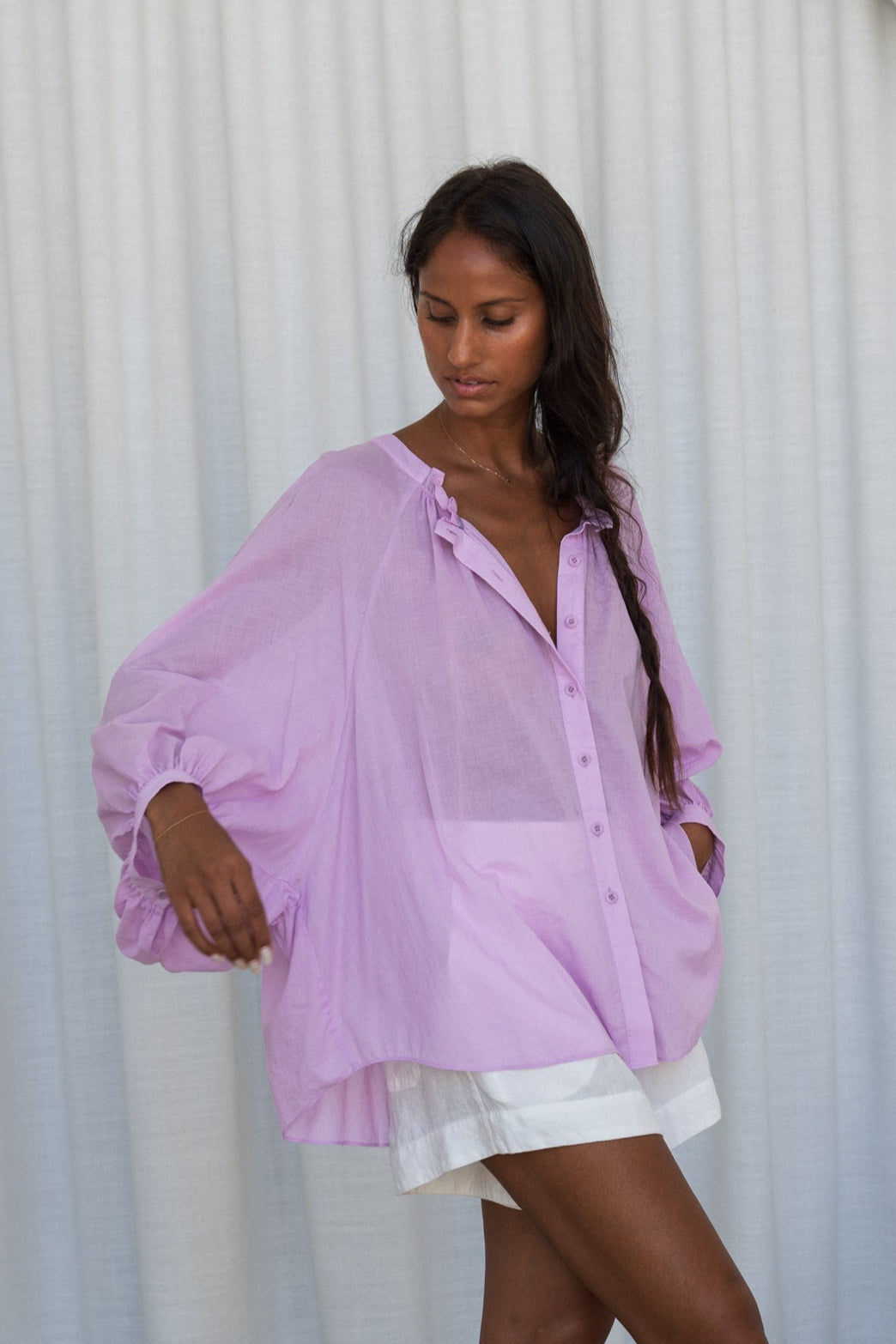 LILLY PILLY woman wearing a orchid Thalia cotton voile shirt  blouse showing side view in front of a curtain background