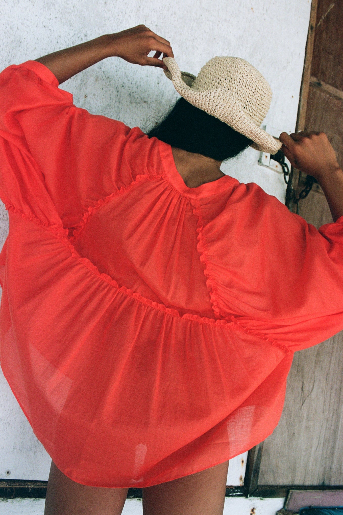 LILLY PILLY woman wearing a spritz Thalia cotton voile shirt holding a straw hat against a white wall.
