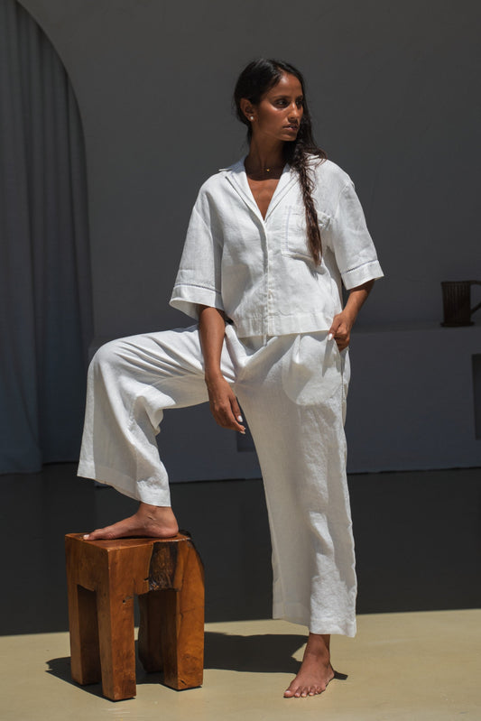 Woman in a ivory Rika linen pants and Quinn shirt standing on a wooden stool in a minimalistic room