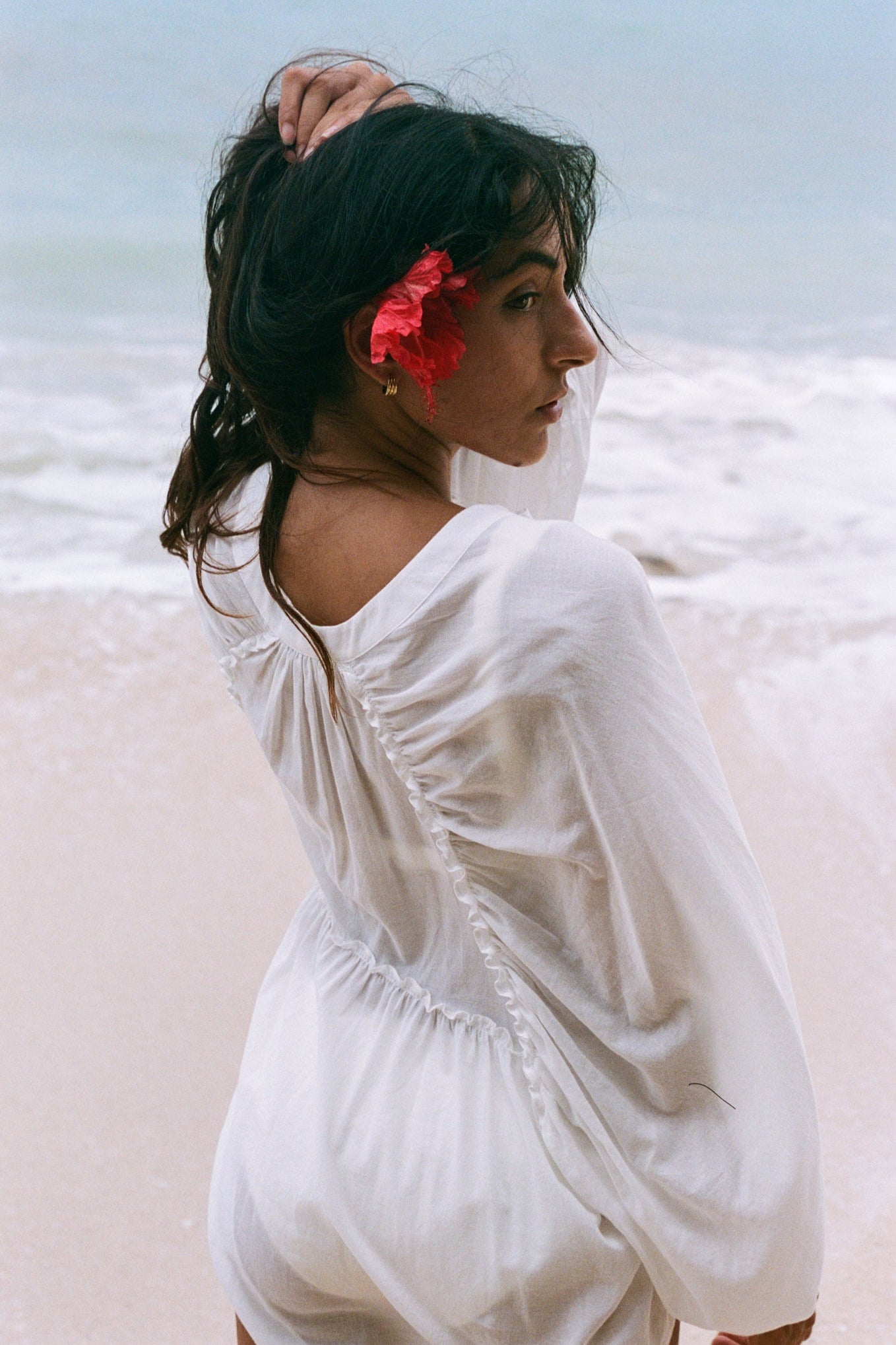 LILLY PILLY woman wearing a ivory Thalia cotton voile shirt blouse with a flower in her hair showing back view while standing by the waters edge