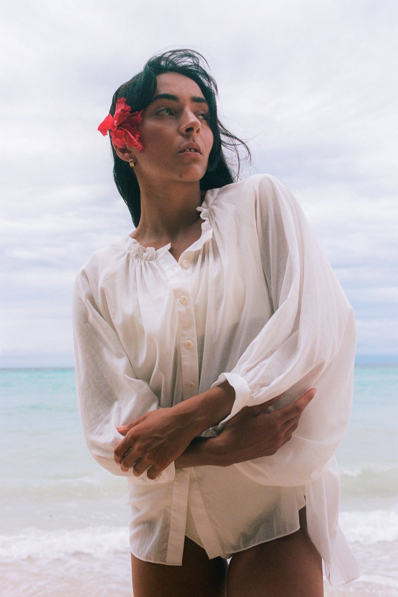 LILLY PILLY woman wearing a ivory Thalia cotton voile shirt blouse with a flower in her hair standing at the waters edge with a blurred background