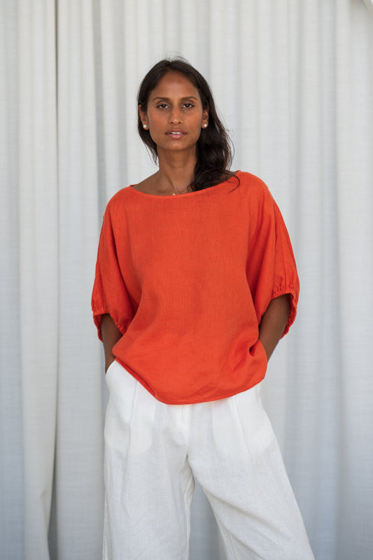 Person wearing a Leia linen top in Spritz and ivory Oli linen pants against a white curtain background